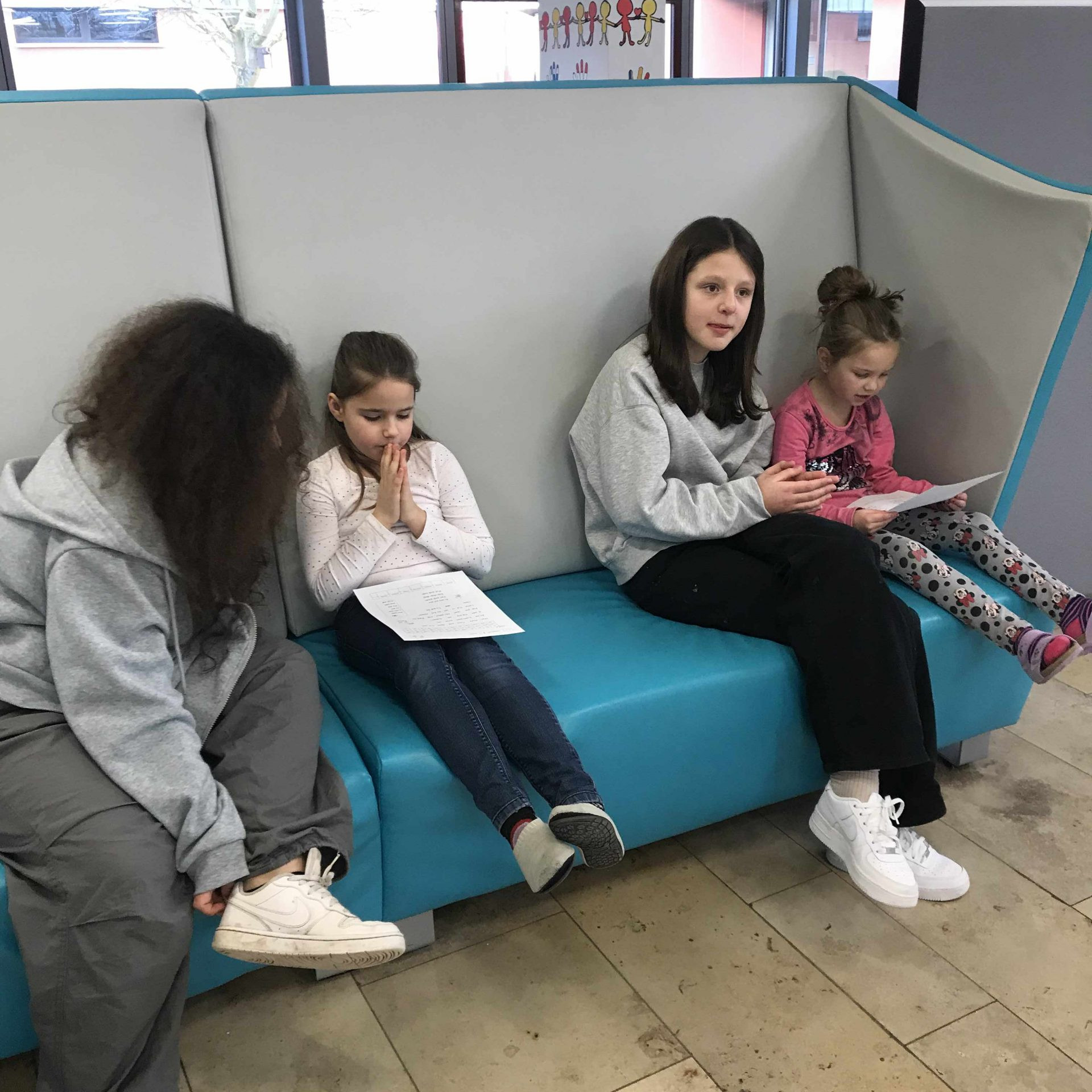 Erstklässlerinnen mit Fibel – Siebtklässlerinnen begleiten – Sofa in der Aula