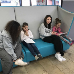 Erstklässlerinnen mit Fibel – Siebtklässlerinnen begleiten – Sofa in der Aula