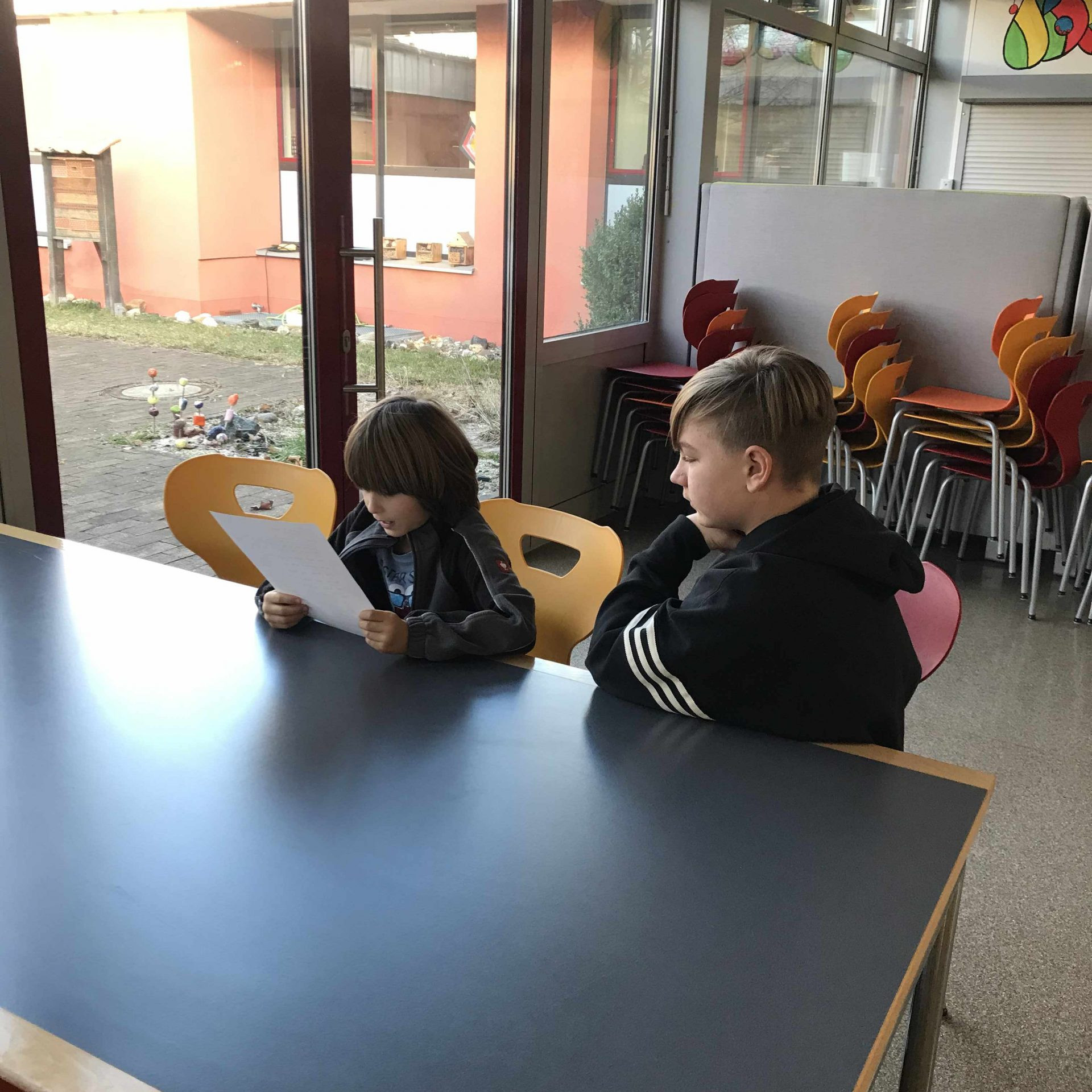 Erstklässler liest konzentriert – Siebtklässler hört zu – Tisch in der Mensa