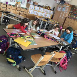 Vier Kinder im Klassenzimmer – Erstklässler lesen aus der Fibel – ältere Schüler unterstützen