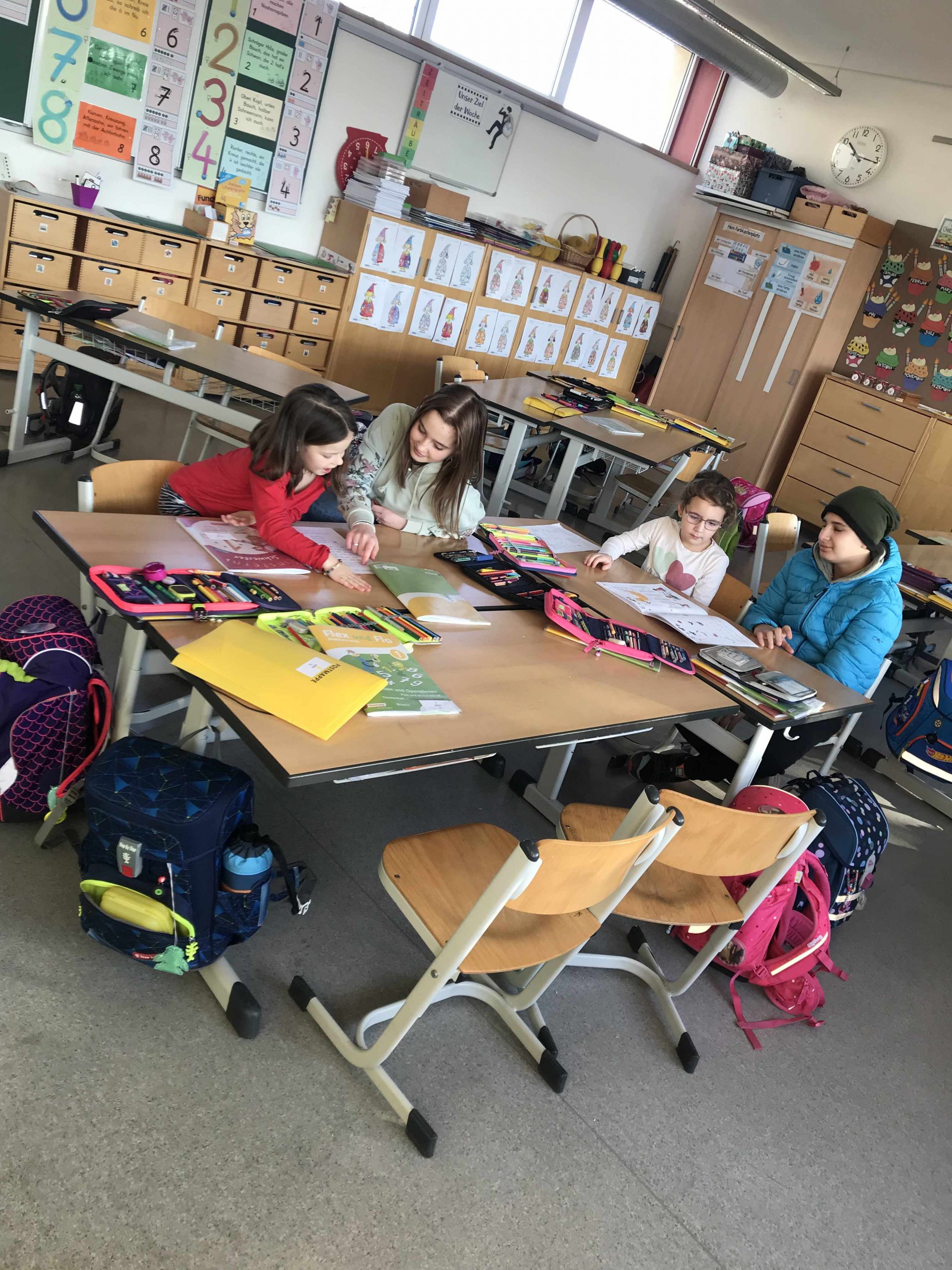 Vier Kinder im Klassenzimmer – Erstklässler lesen aus der Fibel – ältere Schüler unterstützen