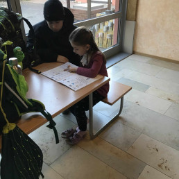 Erstklässlerin liest aus der Fibel – Siebtklässler hört aufmerksam zu – kleine Lesesituation am Tisch