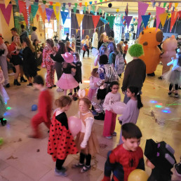 Kinder in unterschiedlichen Kostümen bewegen sich auf einer Tanzfläche mit farbigen Lichtpunkten am Boden.