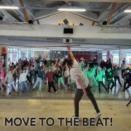 Eine Tanzlehrerin zeigt vor einer großen Schülergruppe Tanzbewegungen in der Aula.
